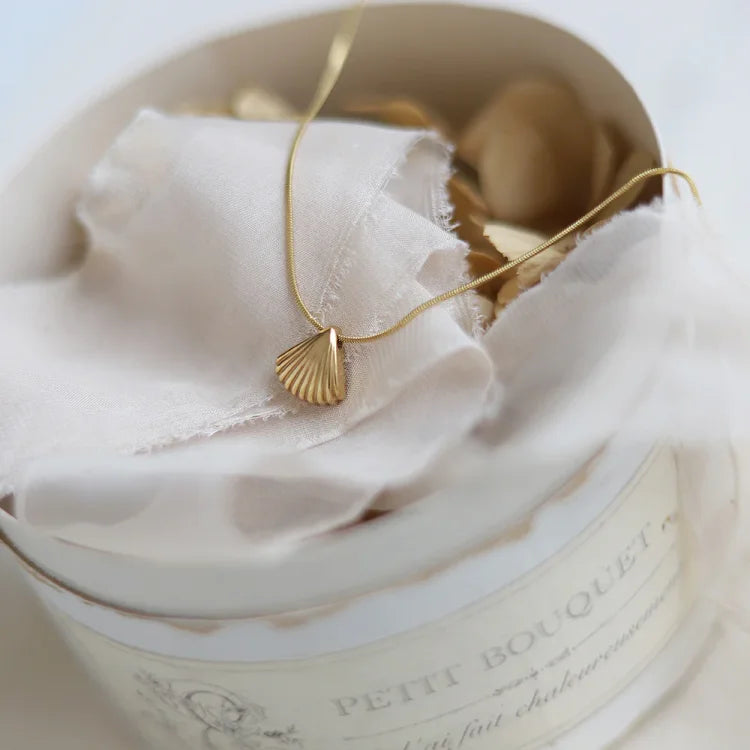 Goldene Muschelkette auf weißem Stoff in runder Schachtel, eleganter Schmuck, Geschenkidee.