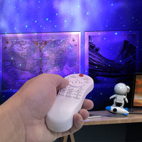 Hand hält Fernbedienung vor Sternenprojektor, Weltkarte und Astronautenfigur im Hintergrund.