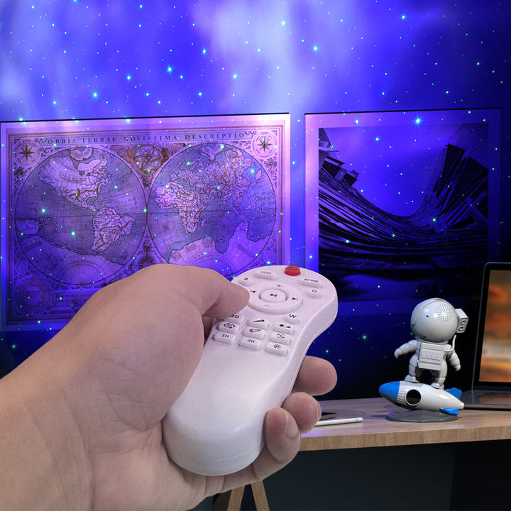 Hand hält Fernbedienung vor Sternenprojektor, Weltkarte und Astronautenfigur im Hintergrund.