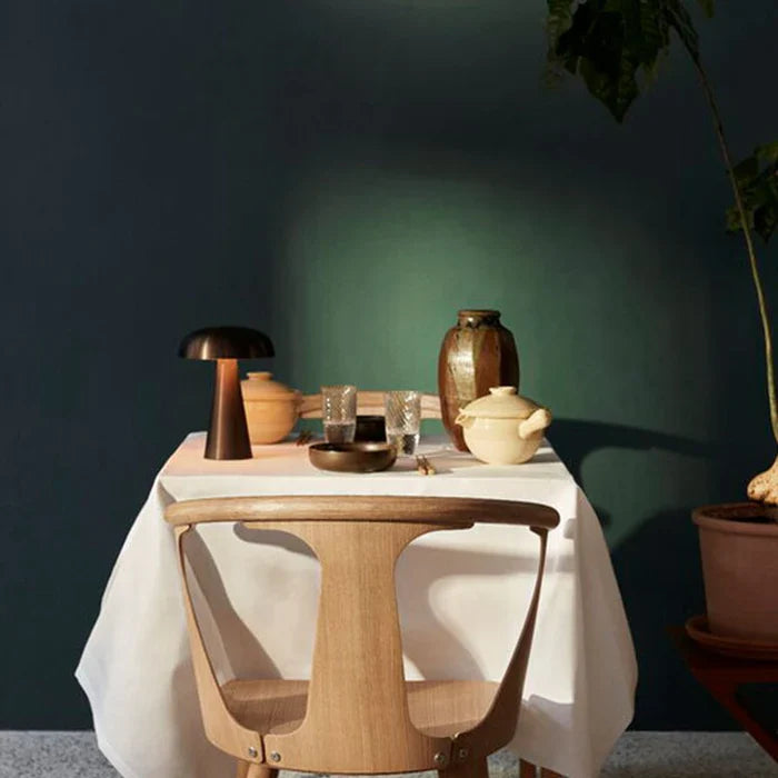 Holztisch mit Keramikgeschirr, Teekanne und Gläsern vor dunkelgrüner Wand, skandinavisches Design.