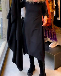 Frau in schwarzem asymmetrischem Kleid, schwarze Stiefel, Modegeschäft, moderne Damenmode.