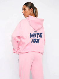 Frau in rosa Hoodie und Jogginghose mit "White Fox" Aufdruck, lässige Damenmode.
