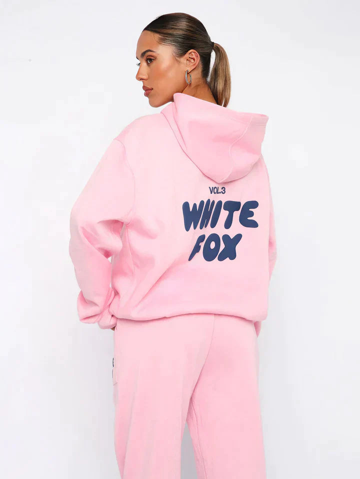 Frau in rosa Hoodie und Jogginghose mit "White Fox" Aufdruck, lässige Damenmode.