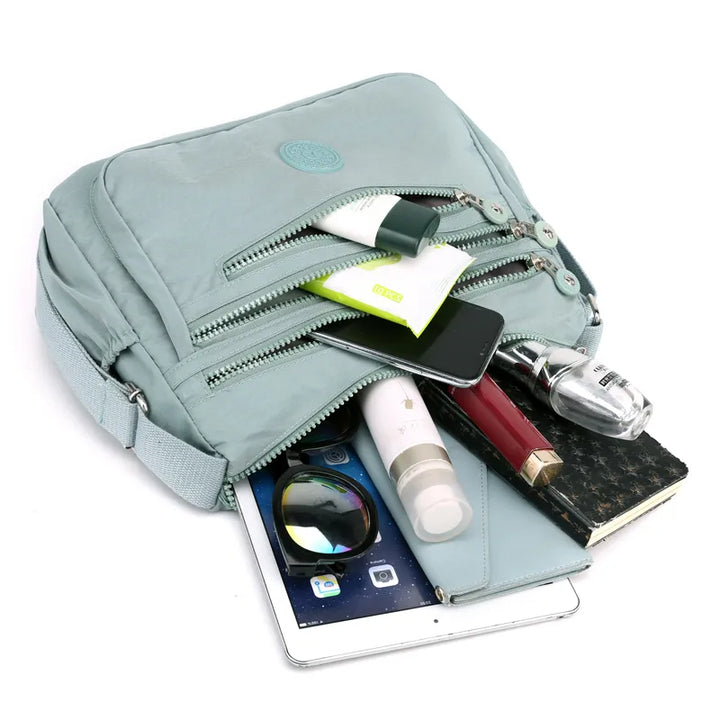 Hellblaue Umhängetasche mit Reißverschlüssen, gefüllt mit Alltagsgegenständen, ideal für Reisen.