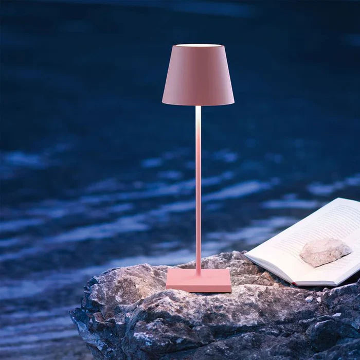 Rosa Tischlampe auf Felsen neben offenem Buch, moderne LED-Beleuchtung, stilvolles Design.