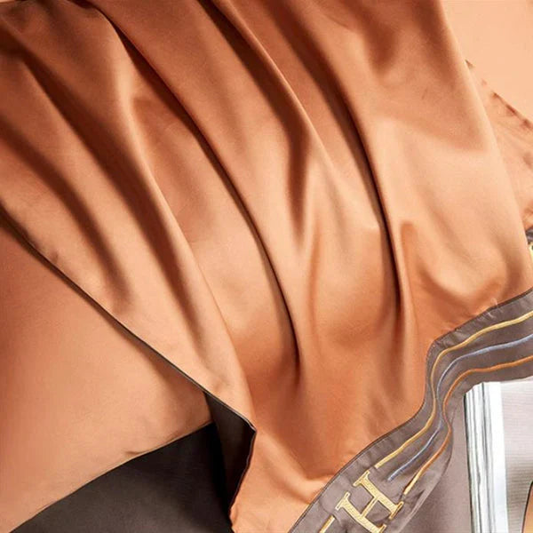 Luxuriöse orangefarbene Seidendecke mit braunem Rand, elegante Heimtextilien, hochwertige Bettwäsche.