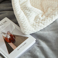 Weiße Strickdecke auf grauem Sofa mit Buch und Teetasse, gemütliche Wohnkultur.