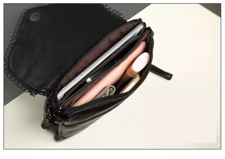 Schwarze Ledertasche mit Reißverschluss, gefüllt mit Kosmetik und Smartphone auf weißem Hintergrund.