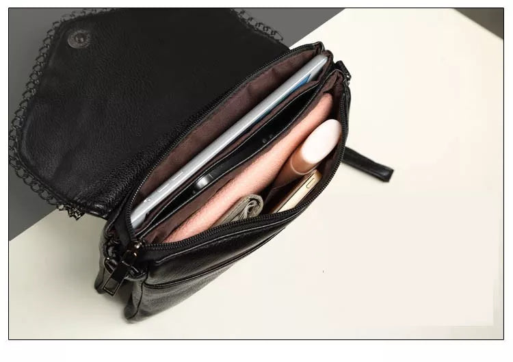 Schwarze Ledertasche mit Reißverschluss, gefüllt mit Kosmetik und Smartphone auf weißem Hintergrund.