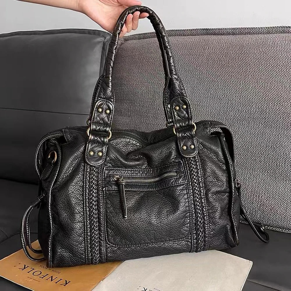 Schwarze Lederhandtasche mit Reißverschluss, modisch, Damenaccessoire, auf grauem Sofa.