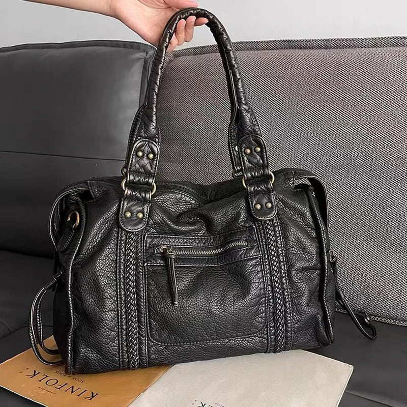 Schwarze Lederhandtasche mit Reißverschluss, modisch, Damenaccessoire, auf grauem Sofa.
