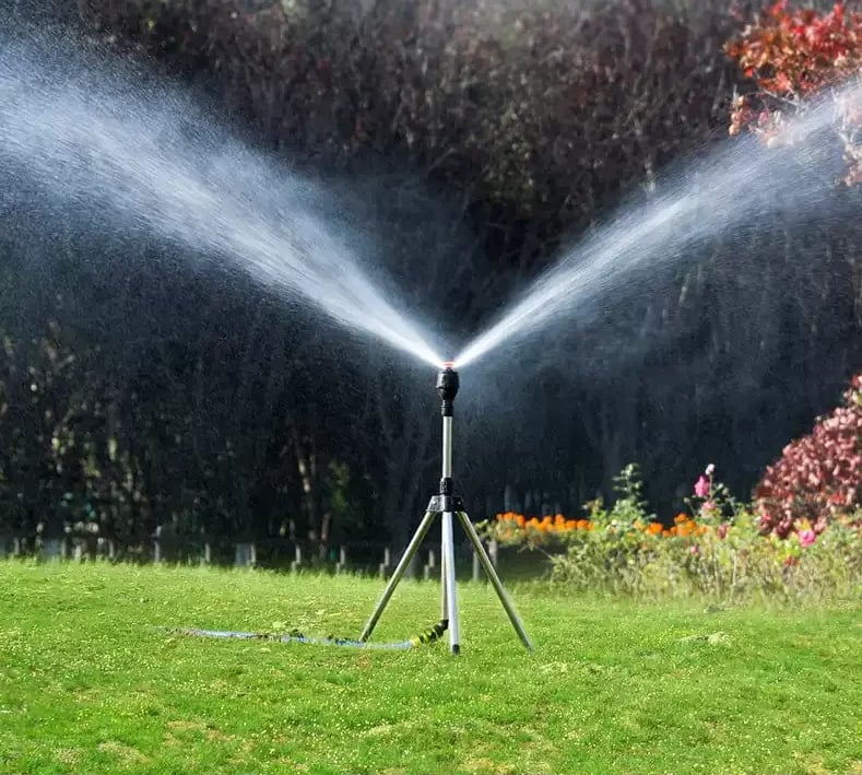 Rasensprenger auf Stativ im Garten, Wasserstrahl, Bewässerung, Sommer, grün, effizient, langlebig.