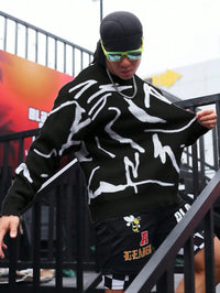 Mann in schwarzem Pullover mit weißem Muster, Sonnenbrille, schwarze Shorts, Treppe hinabsteigend.