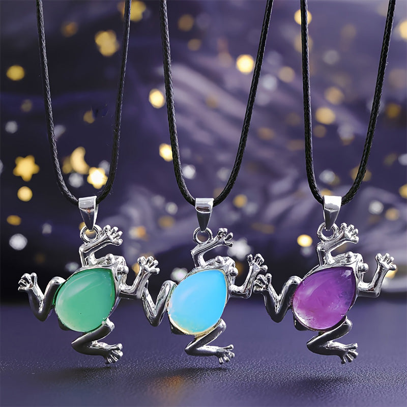 Drei Frosch-Anhänger mit grünen, blauen und lila Edelsteinen an schwarzen Halsketten.