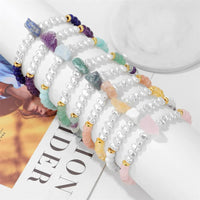 Armbänder mit weißen Perlen, bunten Edelsteinen und goldenen Akzenten auf Marmortisch.