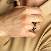 Männerhand mit schwarzem Edelstahlring, goldene Verzierung, elegantes Schmuckdesign.