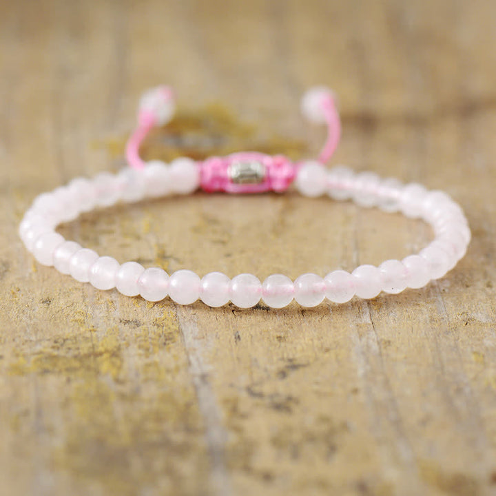 Rosenquarz Armband mit rosa Perlen, verstellbar, auf Holzoberfläche.