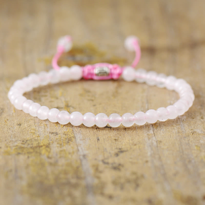 Rosenquarz Armband mit rosa Perlen, verstellbar, auf Holzoberfläche.