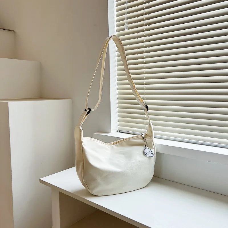 Beige Schultertasche aus Leder auf weißem Tisch vor Jalousie, modisches Accessoire.