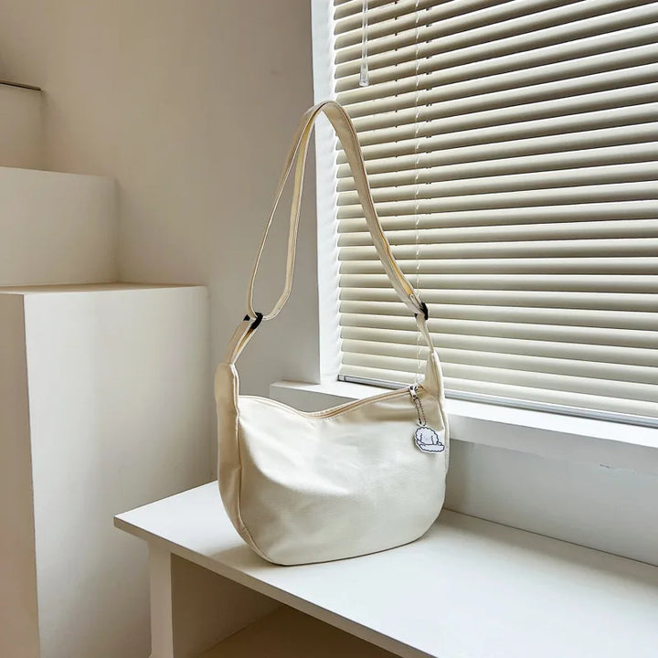 Beige Schultertasche aus Leder auf weißem Tisch vor Jalousie, modisches Accessoire.