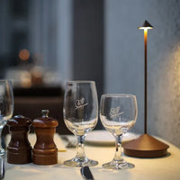 Zwei Weingläser auf gedecktem Tisch mit Pfeffermühlen und Tischlampe, elegantes Restaurantambiente.