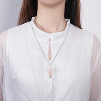 Frau mit weißer Bluse trägt silberne Halskette mit rosa Anhänger.