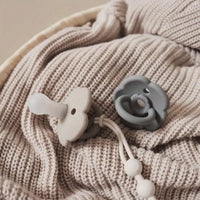 Beige Babydecke mit grauem und weißem Silikon-Schnuller auf Strickstoff.