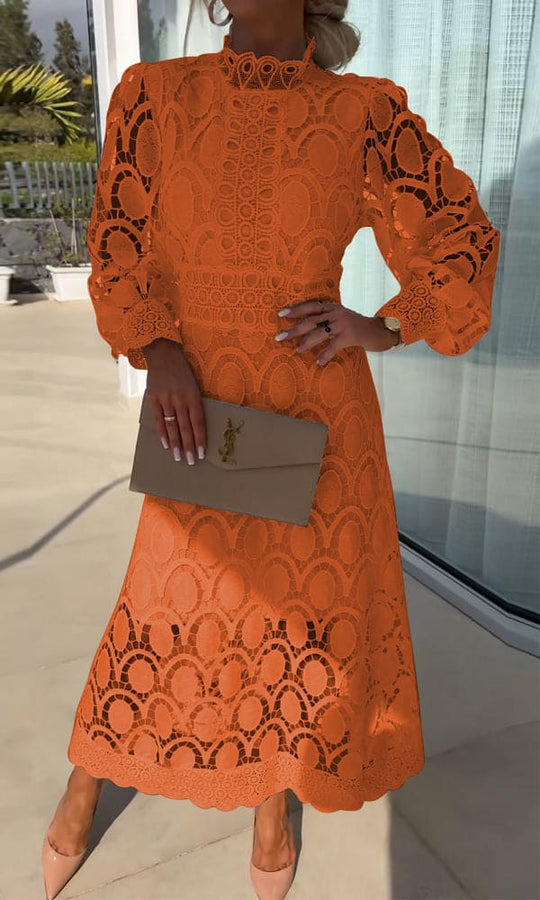 Frau in orangefarbenem Spitzenkleid mit beiger Clutch auf Terrasse bei Tageslicht.