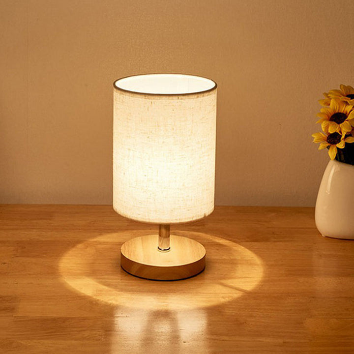 Beige Tischlampe mit Stoffschirm auf Holztisch, moderne Beleuchtung, Inneneinrichtung.