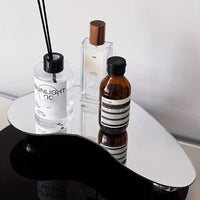 Drei Parfümflaschen auf organisch geformtem Spiegel, modernes Design, minimalistische Dekoration.