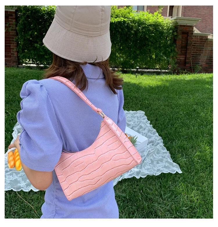 Frau mit rosa Krokodilleder-Handtasche im Park, lila Kleid, beige Hut, Sommermode.