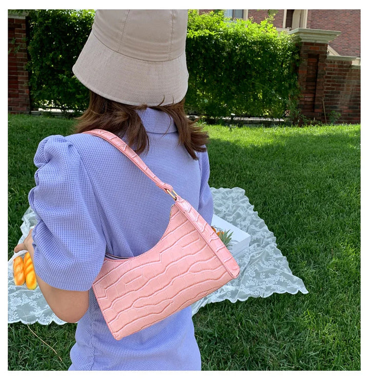 Frau mit rosa Krokodilleder-Handtasche im Park, lila Kleid, beige Hut, Sommermode.
