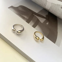 Silber- und goldfarbener offener Ring auf Buch, minimalistisches Schmuckdesign.
