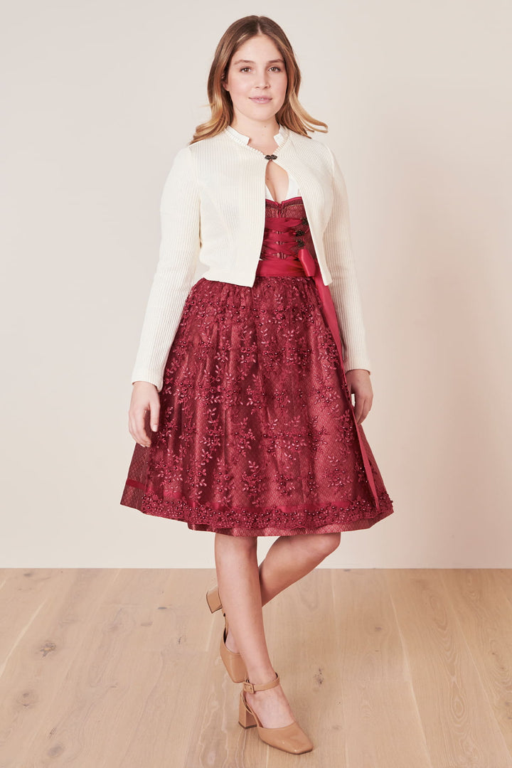 Frau in rotem Spitzenkleid und weißer Strickjacke, elegante Mode, Holzfußboden.