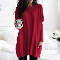 Frau in rotem Oversize-Pullover mit Kaffeetasse, gemütliche Wintermode, Wohnzimmer-Hintergrund.