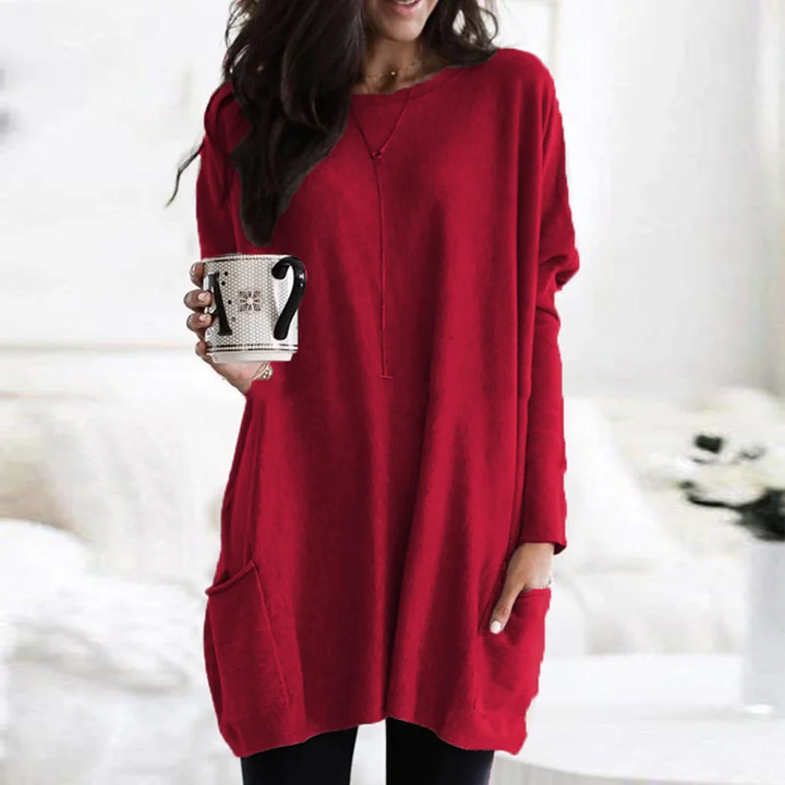 Frau in rotem Oversize-Pullover mit Kaffeetasse, gemütliche Wintermode, Wohnzimmer-Hintergrund.