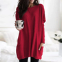 Frau in rotem Oversize-Pullover mit Kaffeetasse, gemütliche Wintermode, Wohnzimmer-Hintergrund.