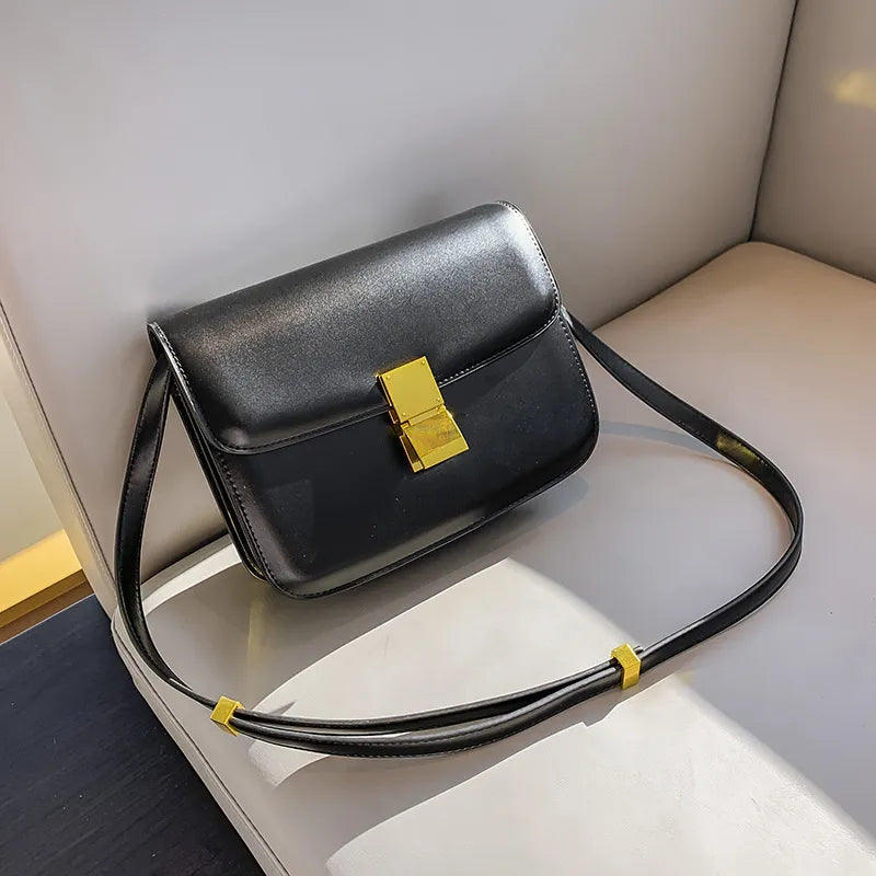 Schwarze Ledertasche mit goldener Schnalle auf weißem Sofa, elegante Damenhandtasche.