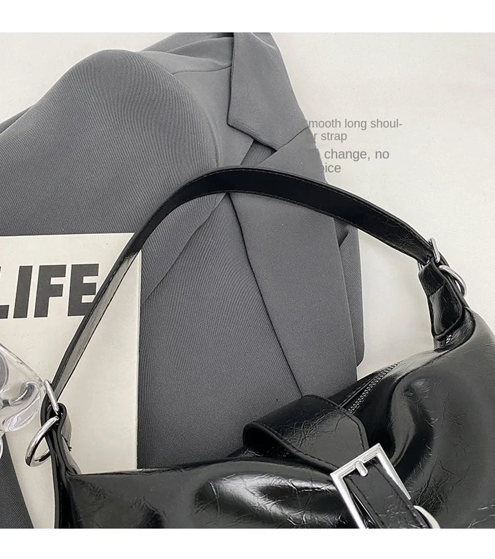 Schwarze Lederhandtasche mit Schnalle auf grauem Blazer, modisch, elegant, Damenaccessoire.