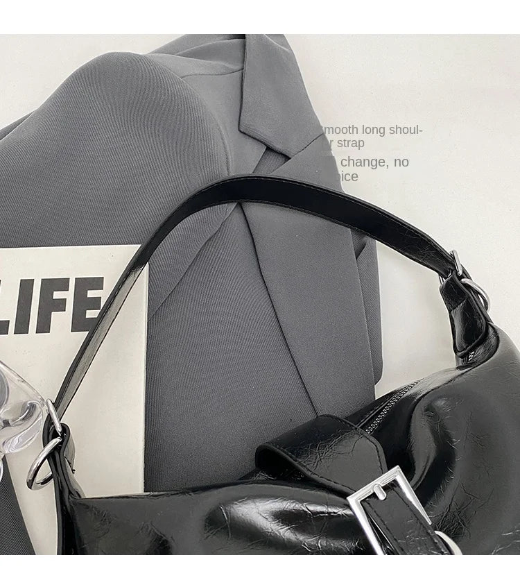 Schwarze Lederhandtasche mit Schnalle auf grauem Blazer, modisch, elegant, Damenaccessoire.