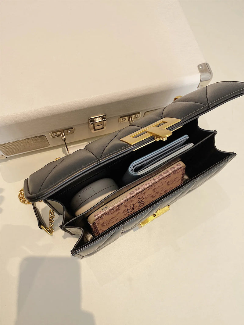 Schwarze Lederhandtasche mit goldener Kette, geöffnet, zeigt Innenfächer und Accessoires.