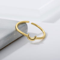 Goldener offener Ring mit Halbmond-Design auf Marmorhintergrund, minimalistischer Schmuck.