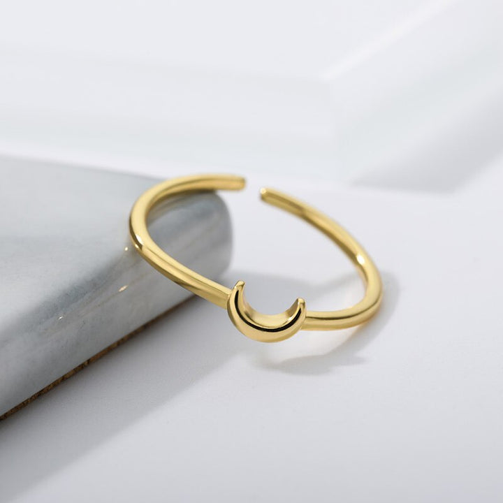 Goldener offener Ring mit Halbmond-Design auf Marmorhintergrund, minimalistischer Schmuck.