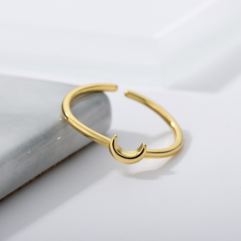 Goldener offener Ring mit Halbmond-Design auf Marmorhintergrund, minimalistischer Schmuck.