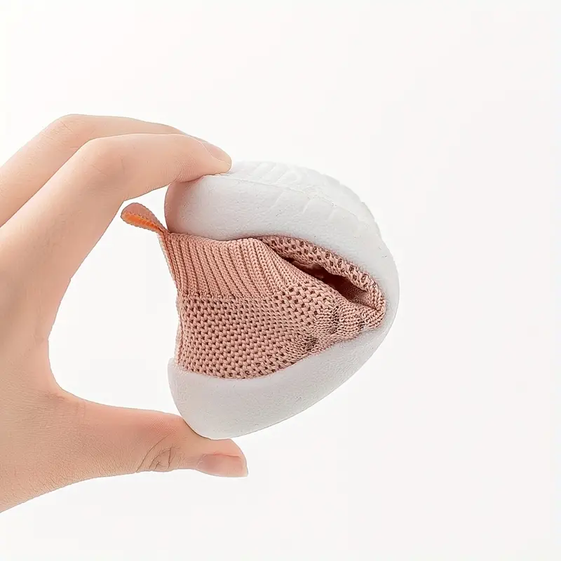 Hand hält flexiblen, rosa Babystrumpf mit weißer Sohle, rutschfest, atmungsaktiv, bequem.