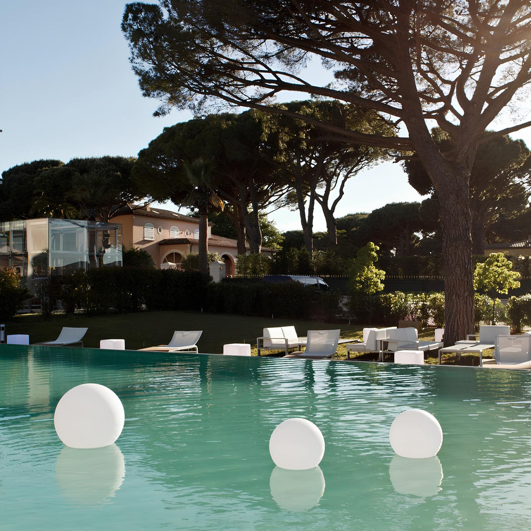 Luxuriöser Pool mit schwimmenden weißen Kugeln, umgeben von eleganten Gartenmöbeln und Bäumen.