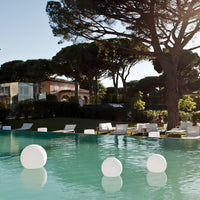 Luxuriöser Pool mit schwimmenden weißen Kugeln, umgeben von eleganten Gartenmöbeln und Bäumen.
