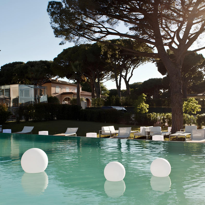 Luxuriöser Pool mit schwimmenden weißen Kugeln, umgeben von eleganten Gartenmöbeln und Bäumen.