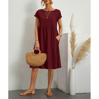 Frau in bordeauxrotem Baumwollkleid, A-Linie, mit Strohtasche, Sommermode, Boho-Stil.