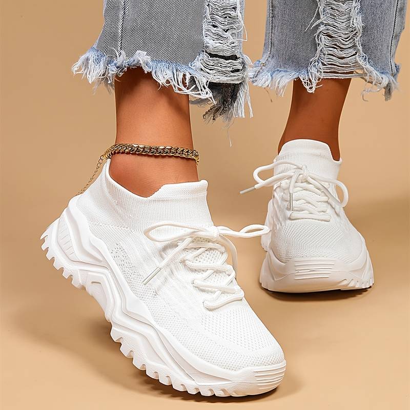 Weiße Damen-Sneaker mit dicker Sohle, gestricktem Obermaterial und zerrissenen Jeans.